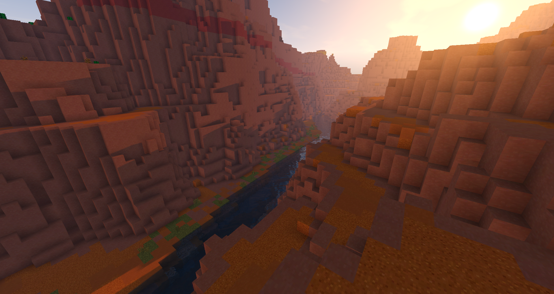 In the image is a canyon shown in the game minecraft. At the bottom of the canyon you can see a river and next to it some grass, while the rest is build our of clay